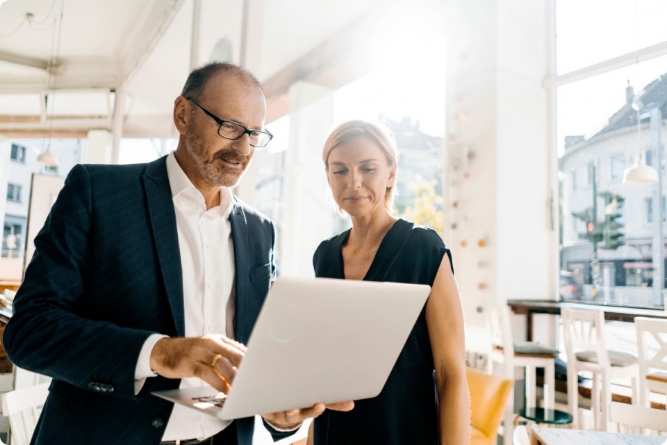 Man in suit and woman in black dress look at a laptop while in a light filled commercial space