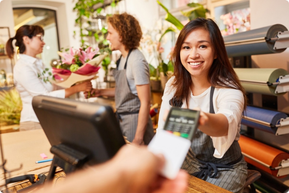 smiling woman in florist takes card payment with mobile eftpos machine while another woman assists a customer in background