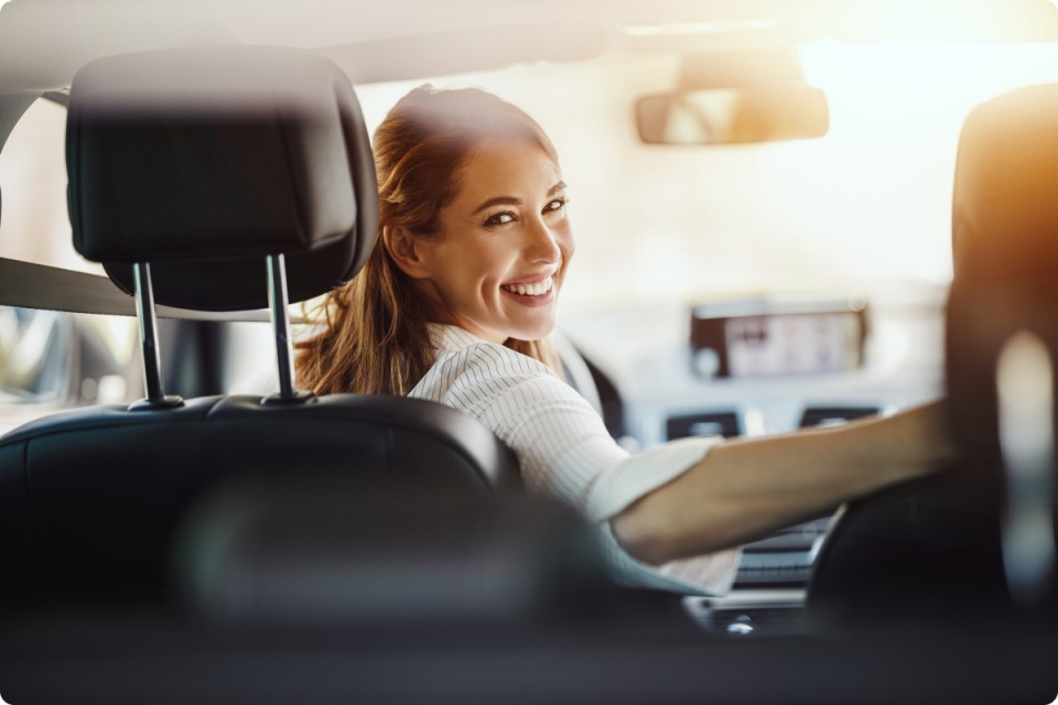 smiling woman in drivers seat of car looks over shoulder