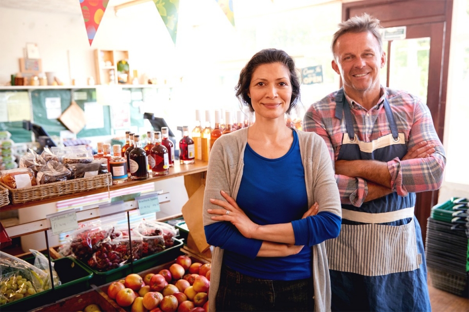 male and female business partners smiling with arms crossed in front of artisan grocery store interior