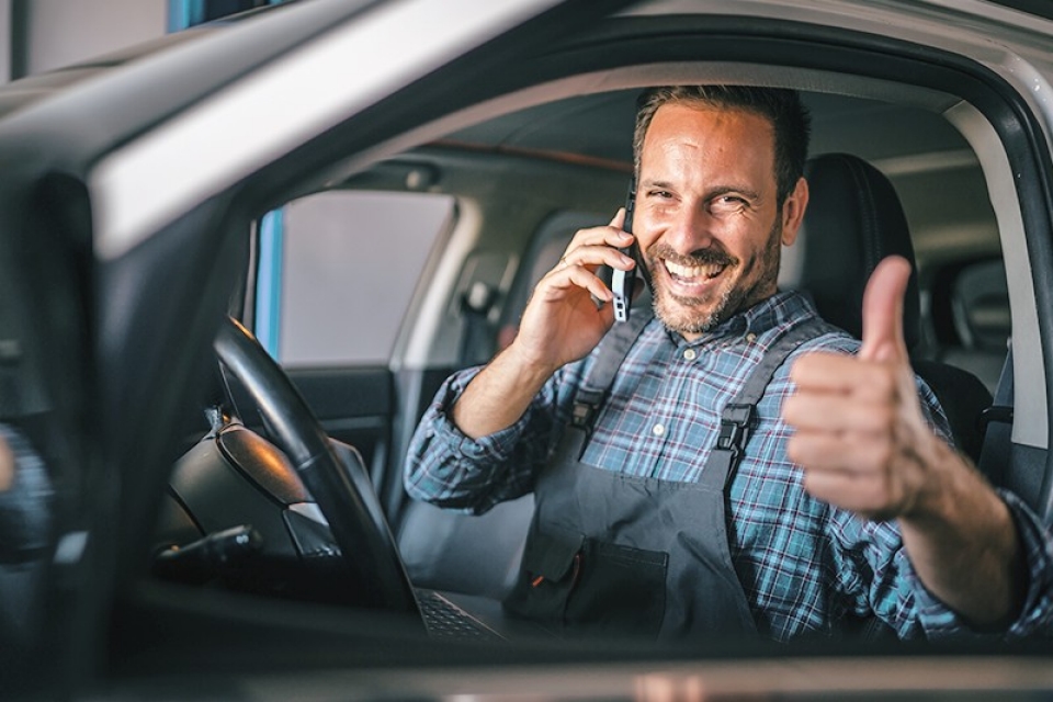 Man sitting in car on mobile phone giving thumbs up sign