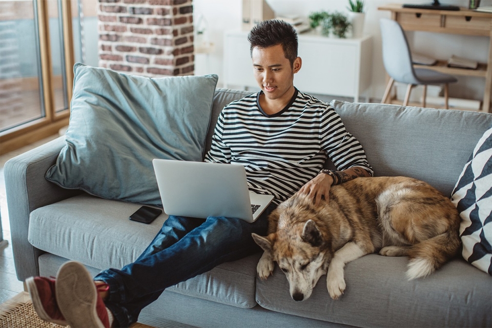 Man sitting on the couch with his laptop and dog
