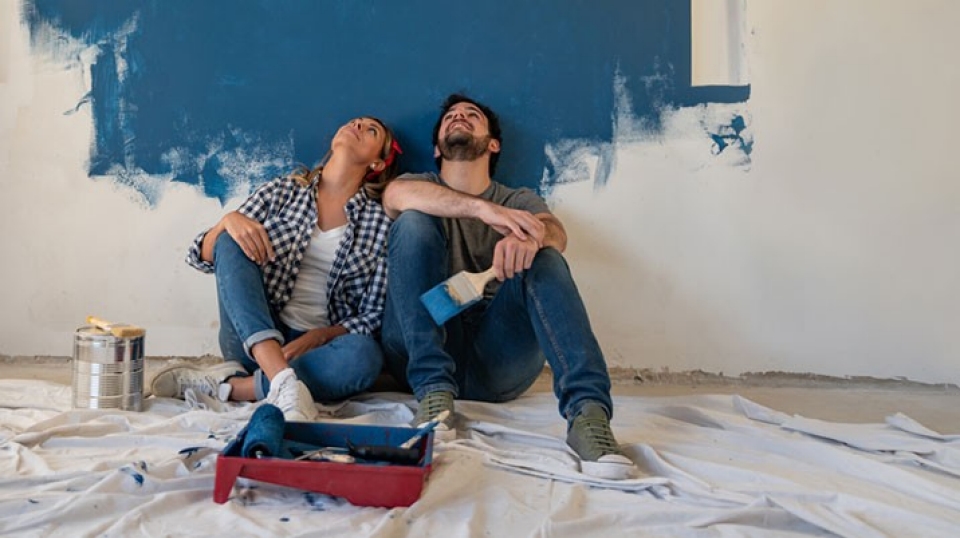 Couple relaxing in front of half painted wall 