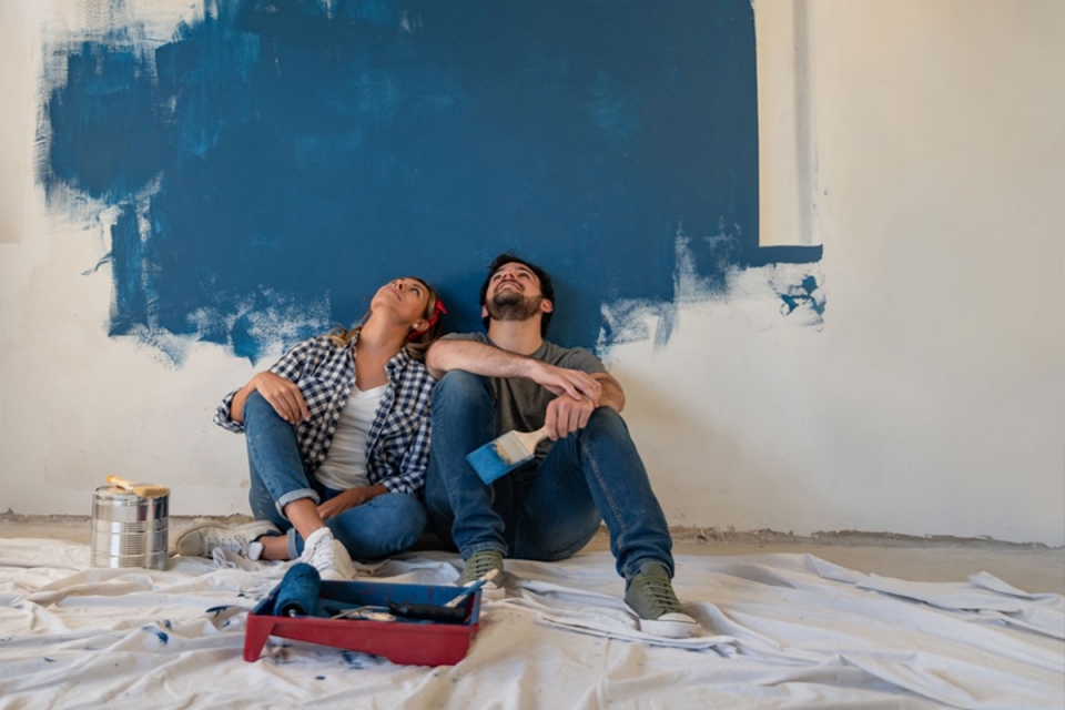 Couple relaxing in front of half painted wall 