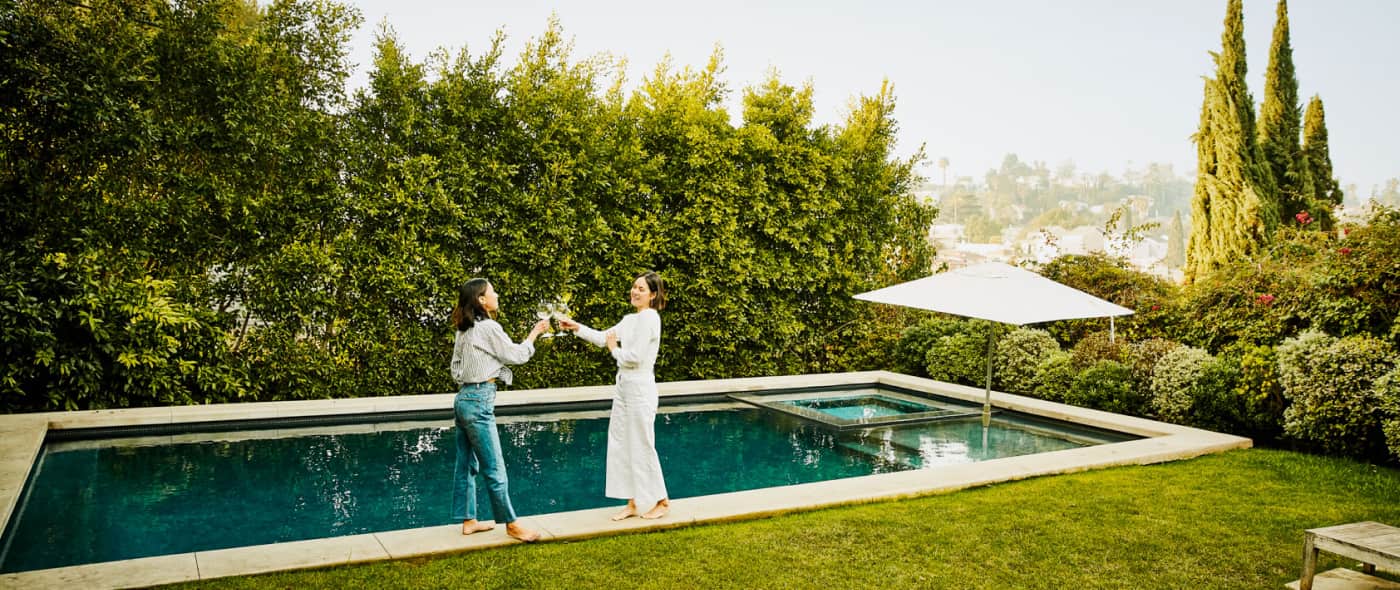 Two ladies clinking wine glasses by a swimming pool
